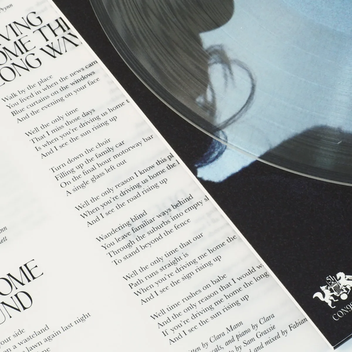Vinyl Cover Artwork with Lyric Insert – Frontside Close-up of vinyl cover artwork with clear record partially covering a printed lyric sheet, highlighting design detail and song text layout.